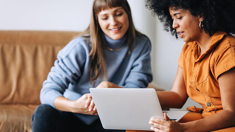 Zwei Frauen sitzen nebeneinander und schauen auf einen Laptop.