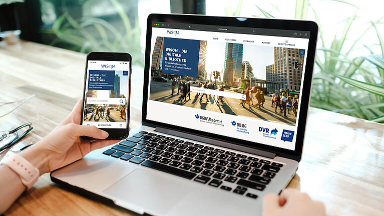 Person hält ein Handy in der Hand und schaut auf einen Laptop