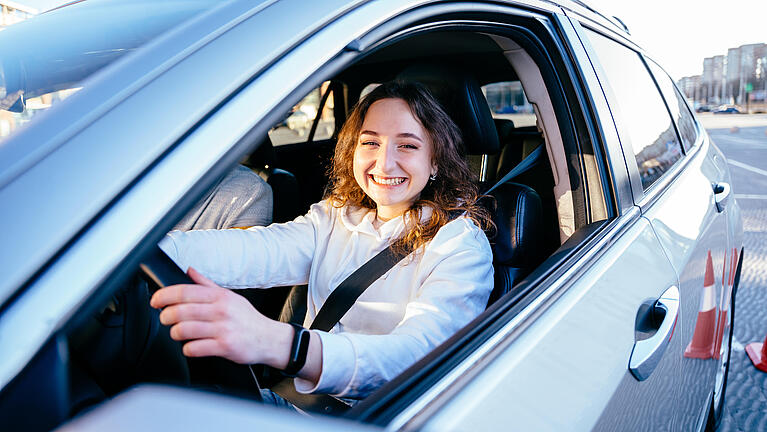 Junge Frau sitz am Steuer im Auto und lächelt.