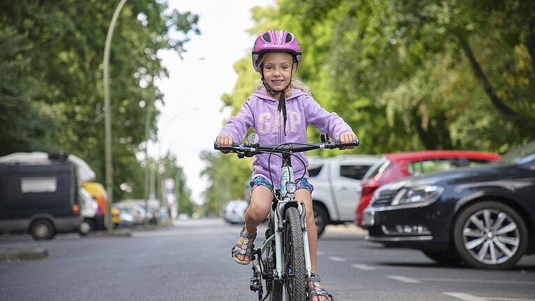 Mädchen fährt lächelnd mit Kinderfahrrad auf der Straße