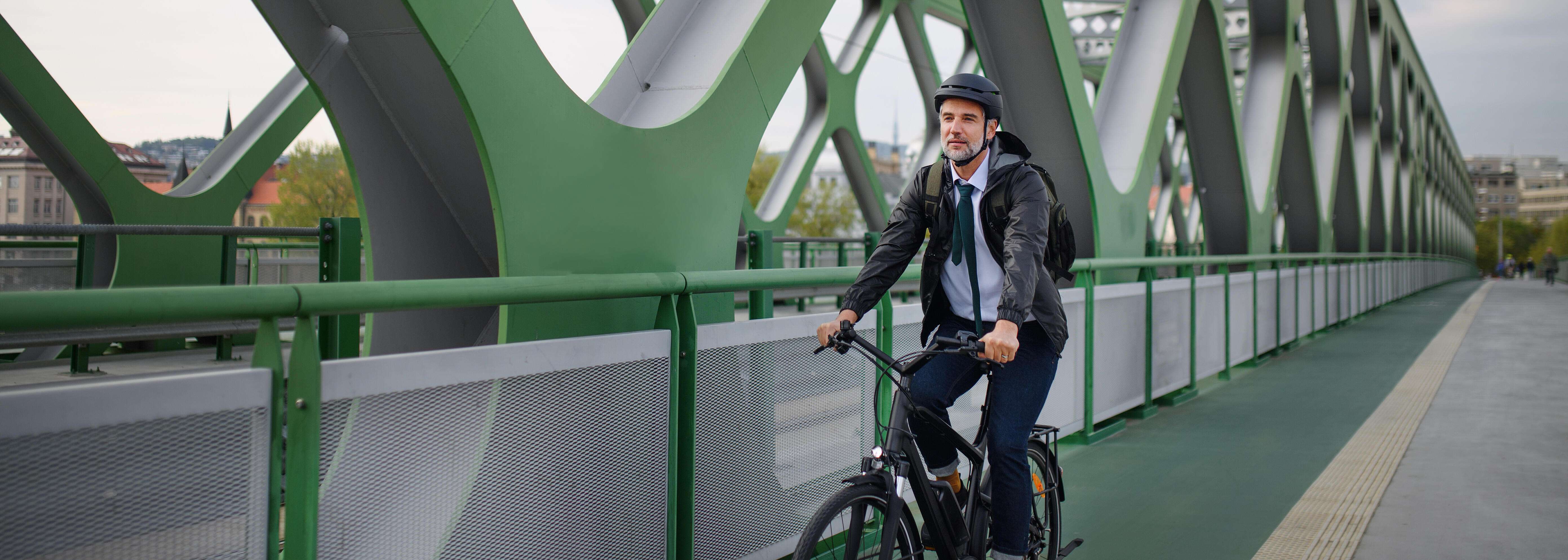Mann in Bürokleidung auf Fahrrad auf grüner Brücke
