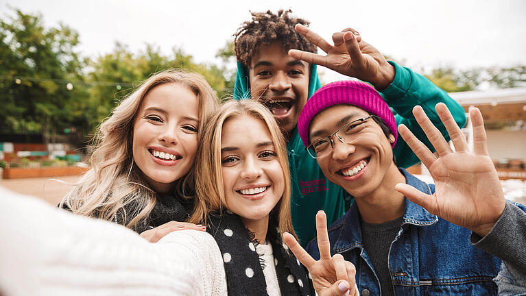 vier Jugendliche, die freundlich in die Kamera grüßen