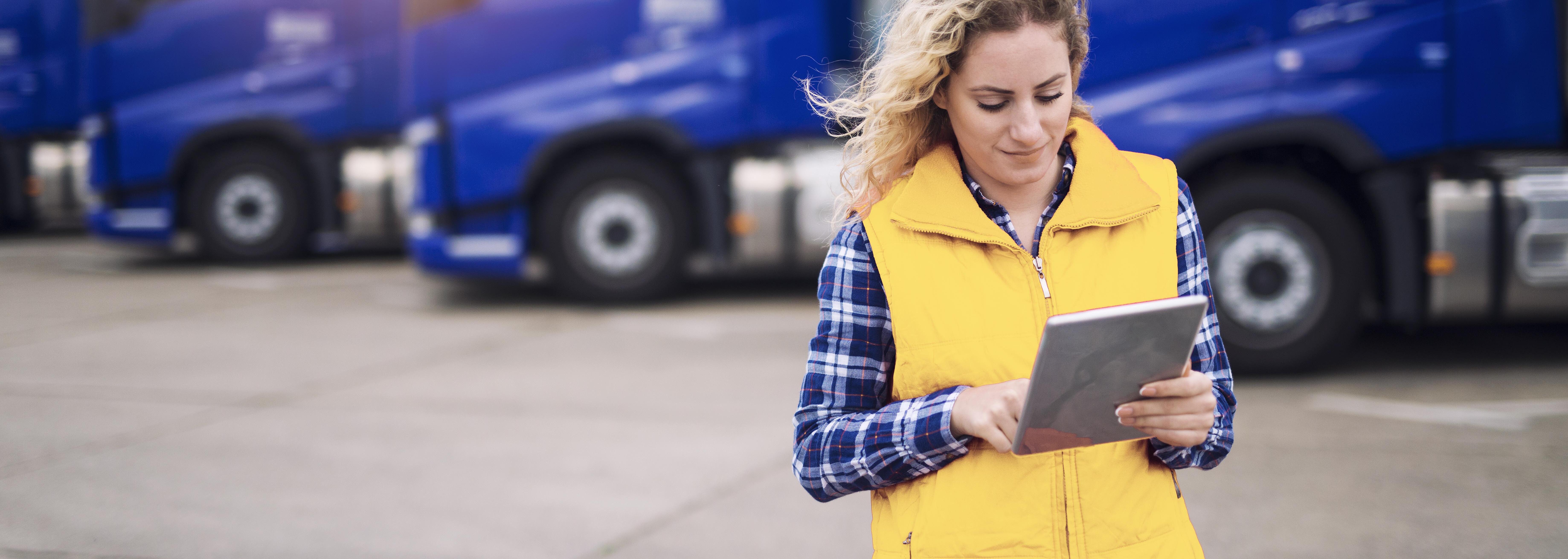 Frau mit Klemmbrett auf Betriebsgelände vor blauer Lkw-Flotte